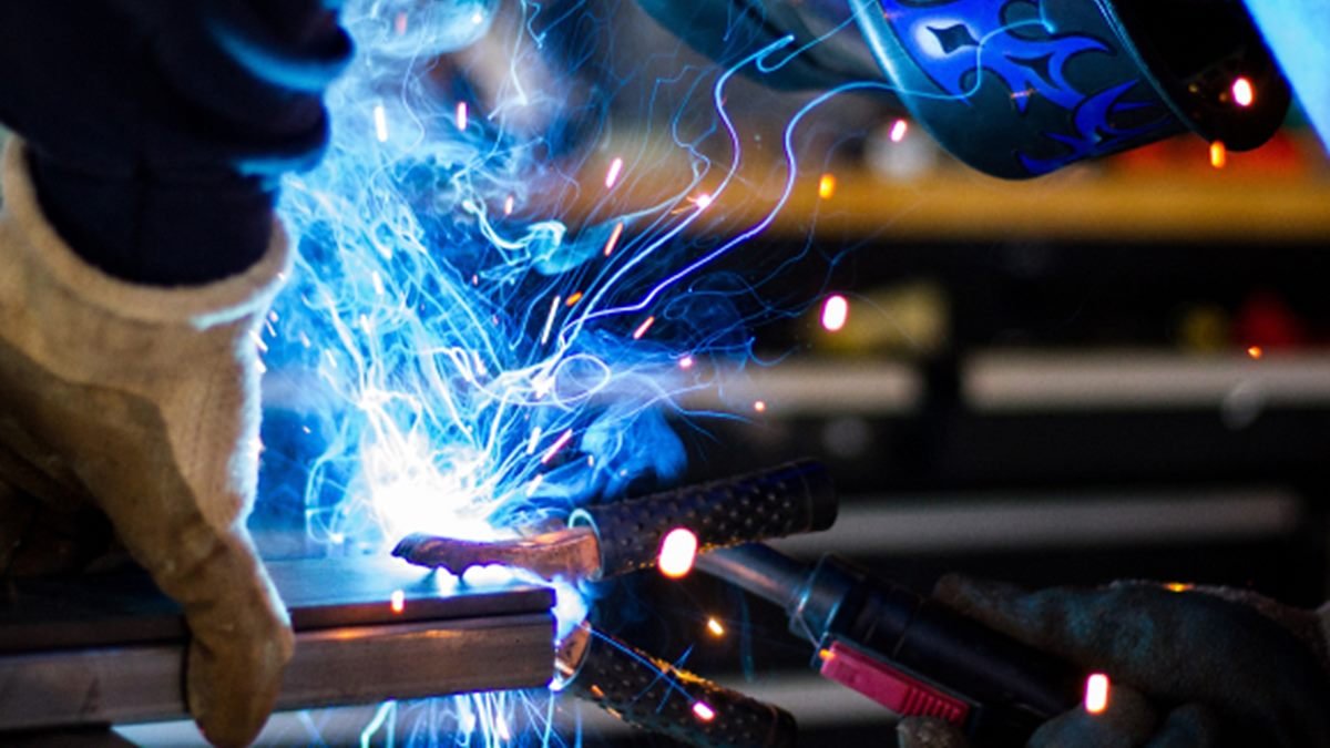 Welder in helmet and gloves welding steel, with sparks flying