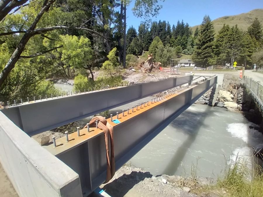 New steel bridge girders spanning a river, with shear studs ready for the deck pour